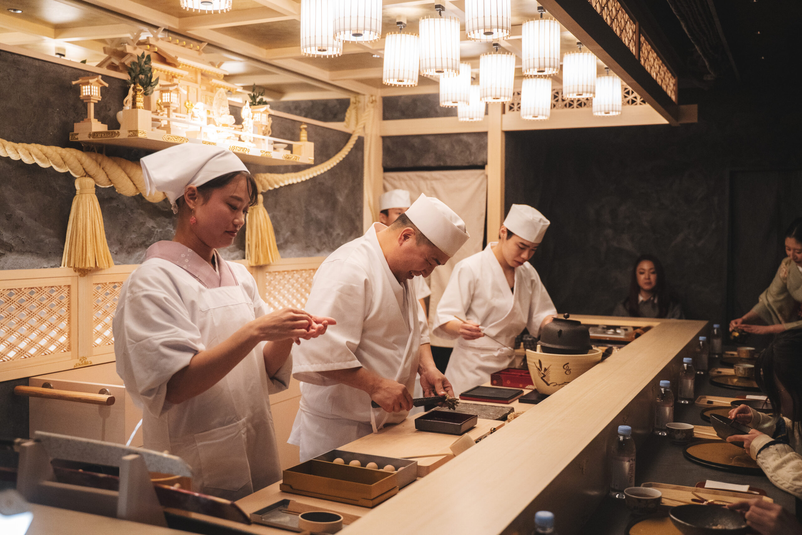 Sushi chefs preparing omakase courses at a live counter with guests seated in front